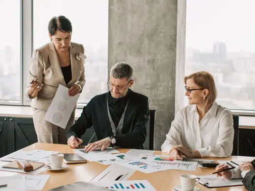 Three business professionals reviewing documents around an office table.