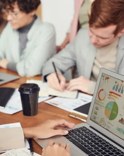 Professionals reviewing charts on a laptop during an office discussion.
